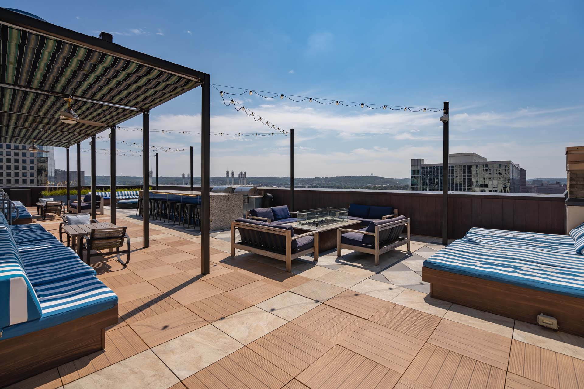 Rooftop lounge with striped daybeds, seating areas, and city views under a blue sky